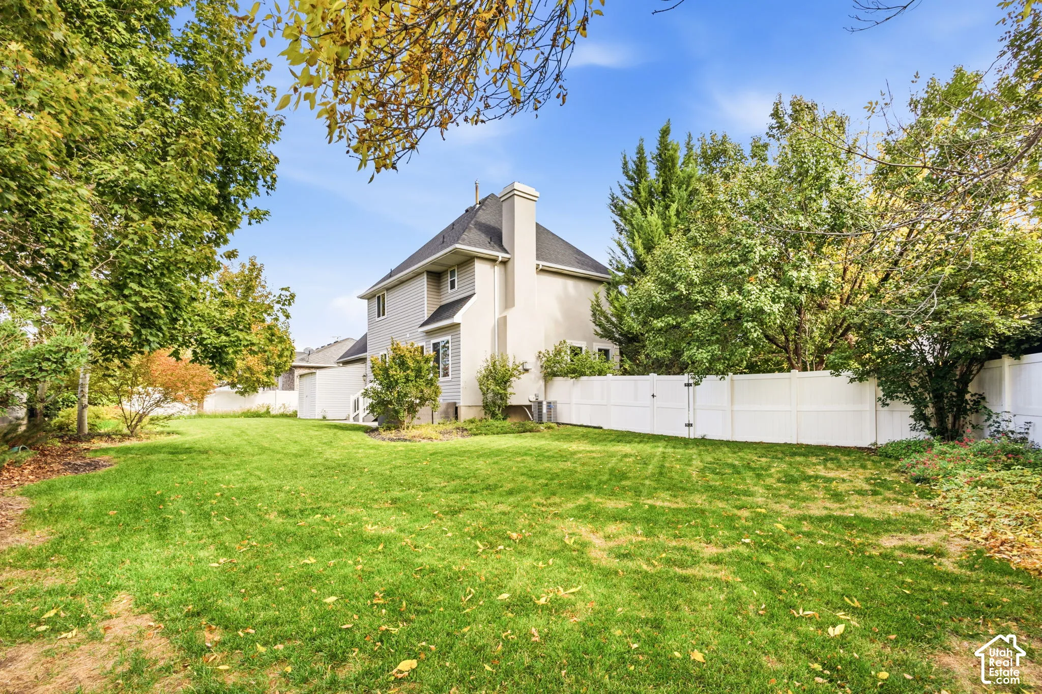 Expansive backyard featuring a manicured lawn, perimeter white vinyl fencing, and mature trees
