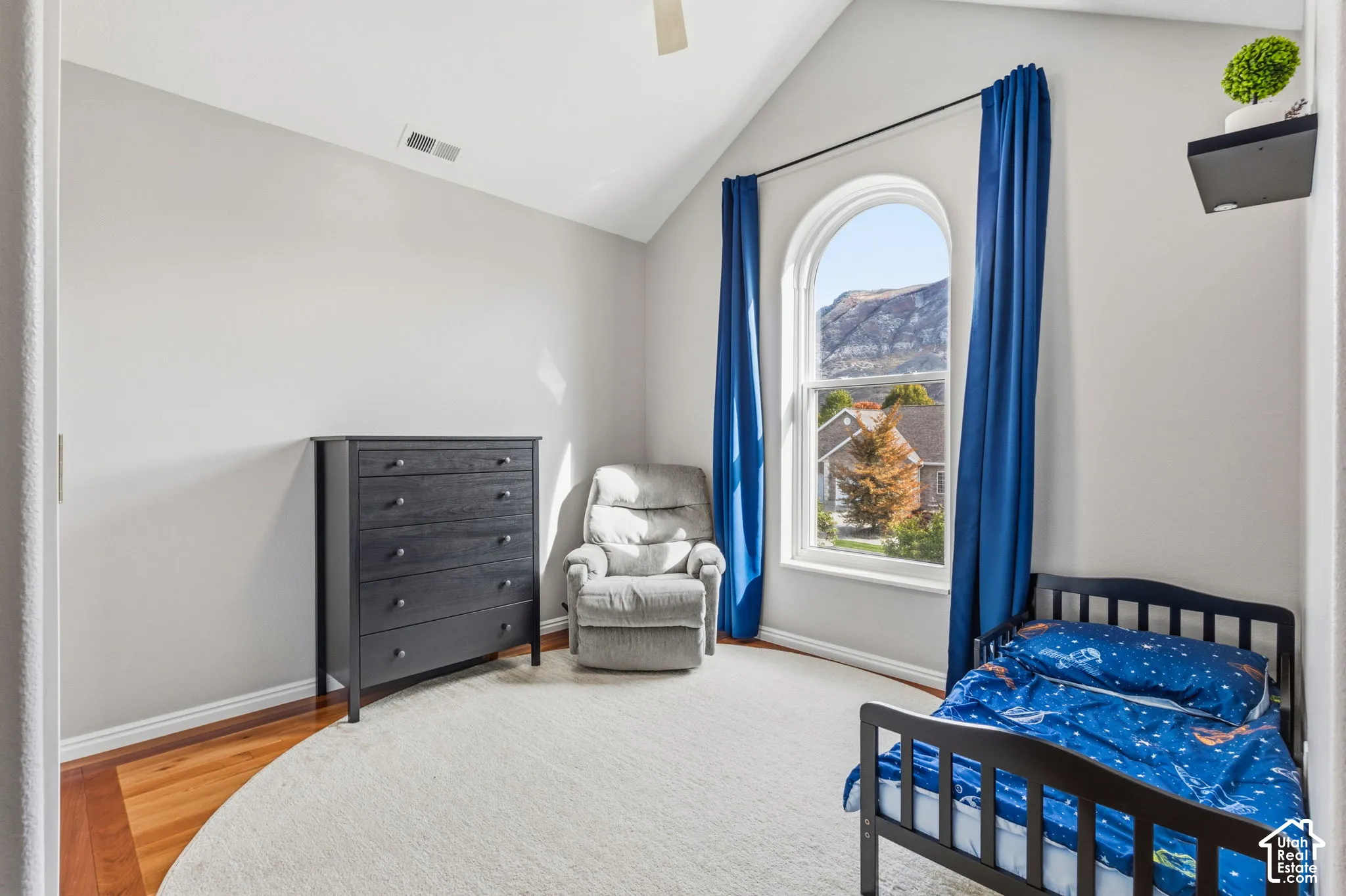 Vaulted ceiling featuring a ceiling fan, wood-finish flooring, and an arched window with mountain scenery