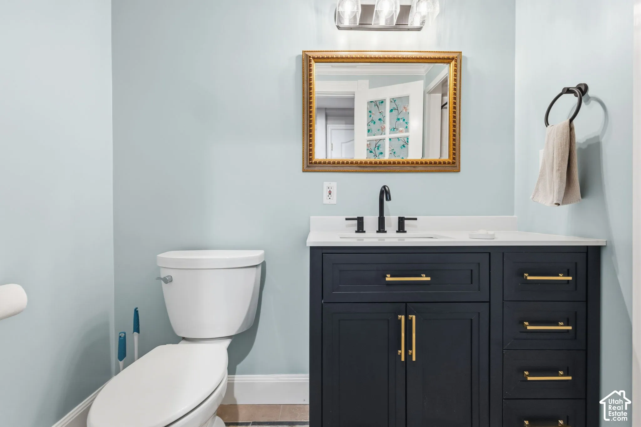 Dark navy vanity featuring gold-tone hardware, a white solid-surface countertop, an undermount sink with a matte black widespread faucet, and a three-light glass fixture