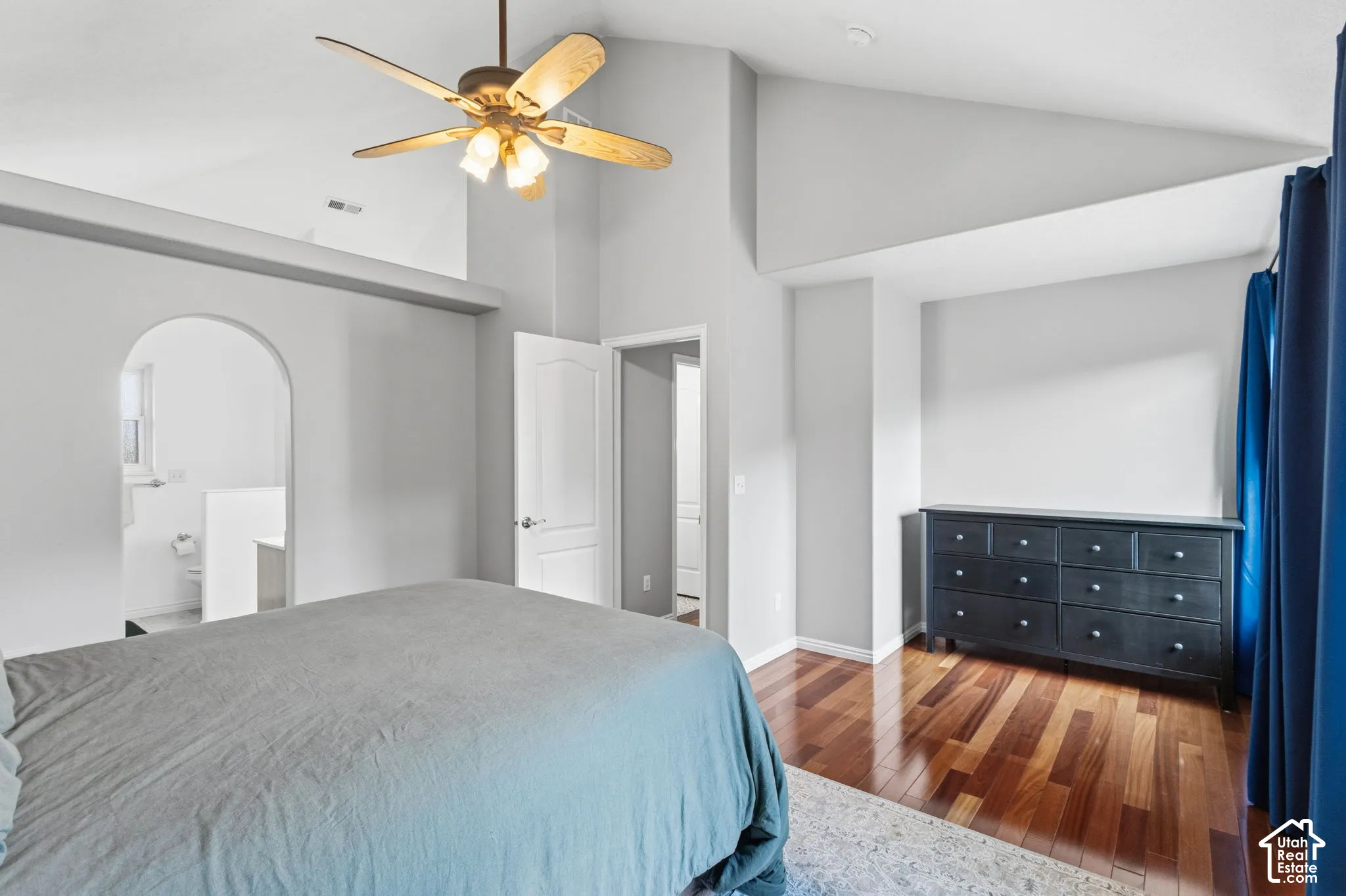Vaulted ceiling, wood-finish flooring, ceiling fan with integrated lighting, and arched doorway