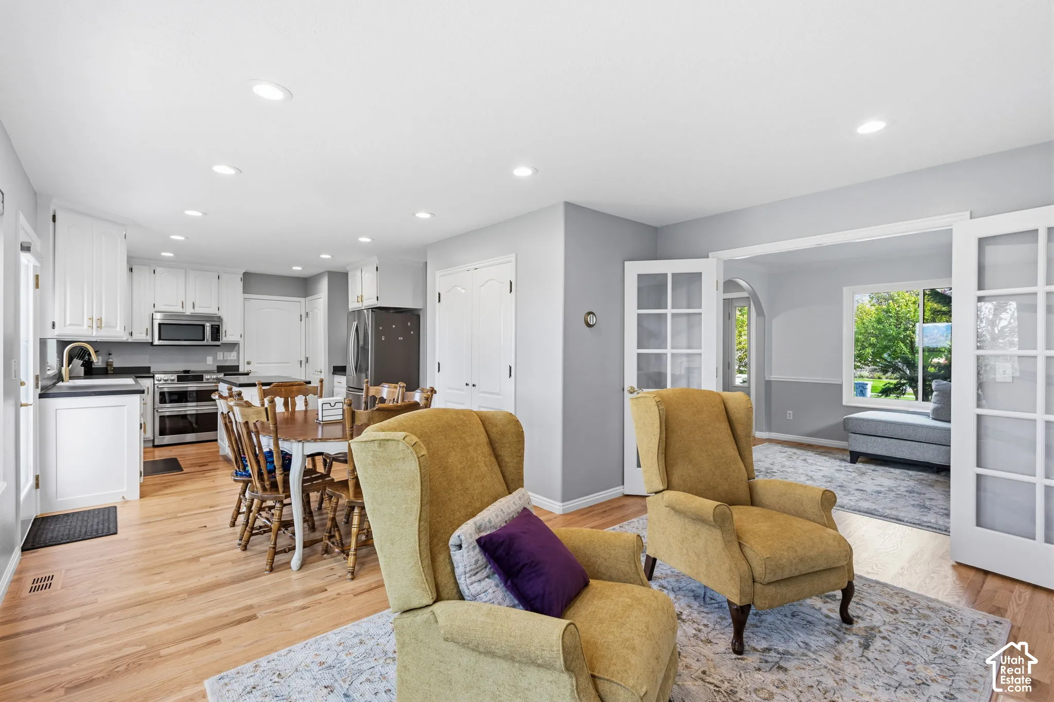 Open-concept kitchen featuring white shaker-style cabinetry, stainless steel appliances, wood-finish flooring, recessed lighting, and white French doors
