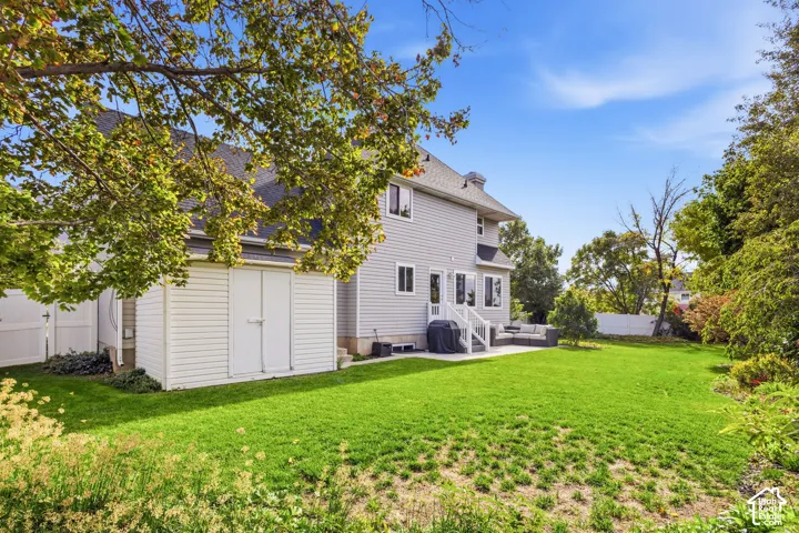 Expansive backyard featuring a level lawn, mature trees, a concrete patio, and white vinyl perimeter fencing
