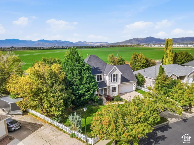 Two-story residence with a stone and siding exterior, multi-pitched roofline, an attached two-car garage, and white picket fencing against a mountain backdrop