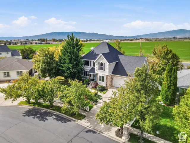 Two-story residence featuring a multi-gabled roofline, stone veneer accents, an attached multi-car garage, mature landscaping, and a mountain backdrop