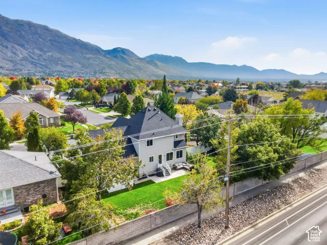 Two-story residence featuring grey lap siding, an asphalt shingle roof, a chimney, and a private rear lawn enclosed by a masonry wall, set against a prominent mountain backdrop