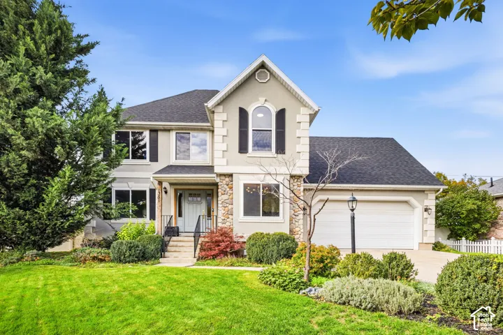 Two-story exterior featuring stone veneer accents, an arched upper-level window, shutters, a multi-gabled roofline, and an attached two-car garage