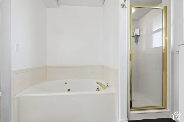 Built-in jetted soaking tub with tile surround, paired with a separate stall shower featuring a metal-framed glass enclosure and gold-toned hardware