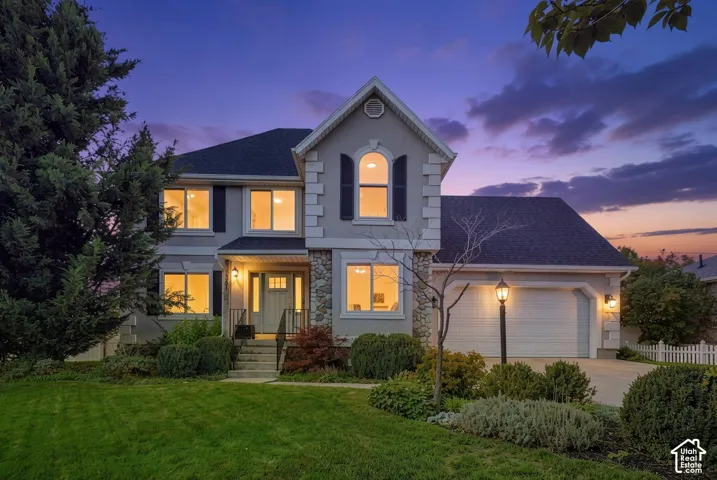 Multi-story residence with a stone veneer facade, gabled roofline, arched upper-level window, attached garage, and manicured landscaping