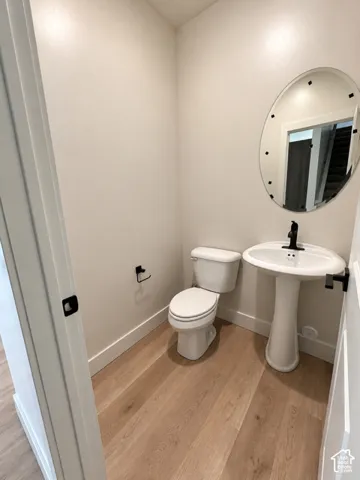 Pedestal sink with matte black faucet, oval wall-mounted mirror, wood-finish flooring, and matte black hardware