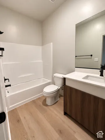 Bathroom featuring wood-finish cabinetry, white countertop with integrated sink, matte black faucet, wall-spanning vanity mirror, and wood-finish flooring