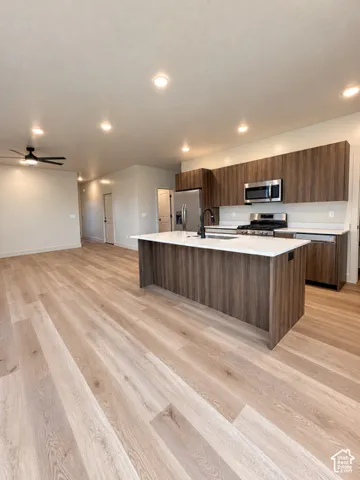 Kitchen featuring wood-finish cabinetry, white countertops, a center island with an integrated sink, stainless steel appliances, and wood-finish flooring