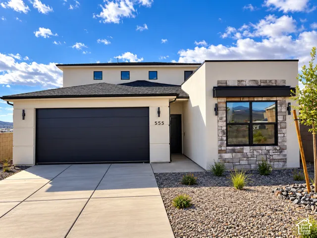 Contemporary exterior featuring smooth stucco siding, stone veneer accents, multi-level roofline, concrete driveway, and attached two-car garage