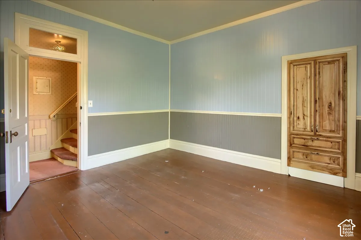 Hardwood flooring, painted wainscoting, light blue wall panels, wood paneled storage cabinet, and interior doorway with transom window