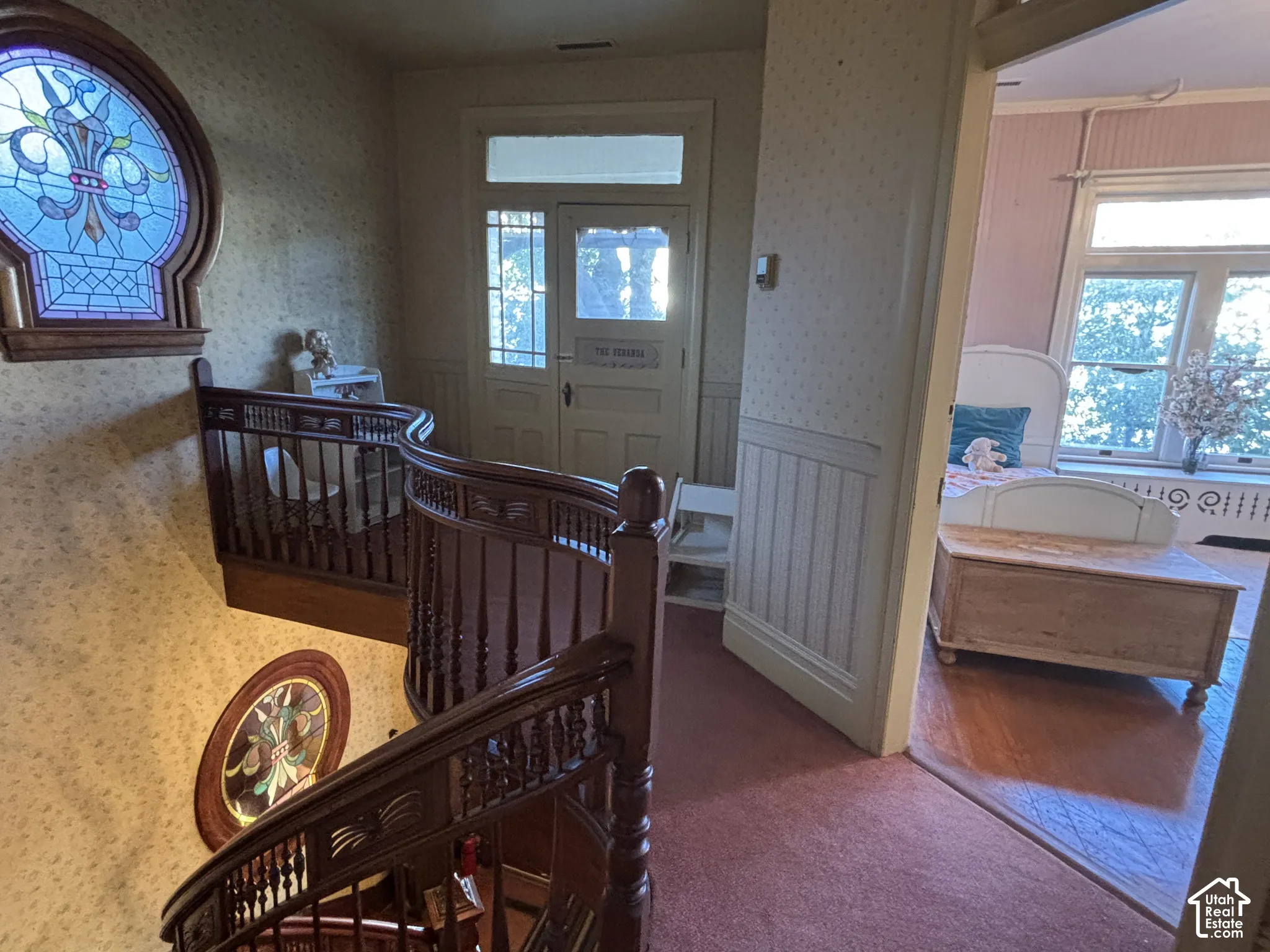 Curved wooden staircase featuring turned balusters, decorative stained glass windows, wood-paneled wainscoting, and a multi-pane glass entryway door with transom