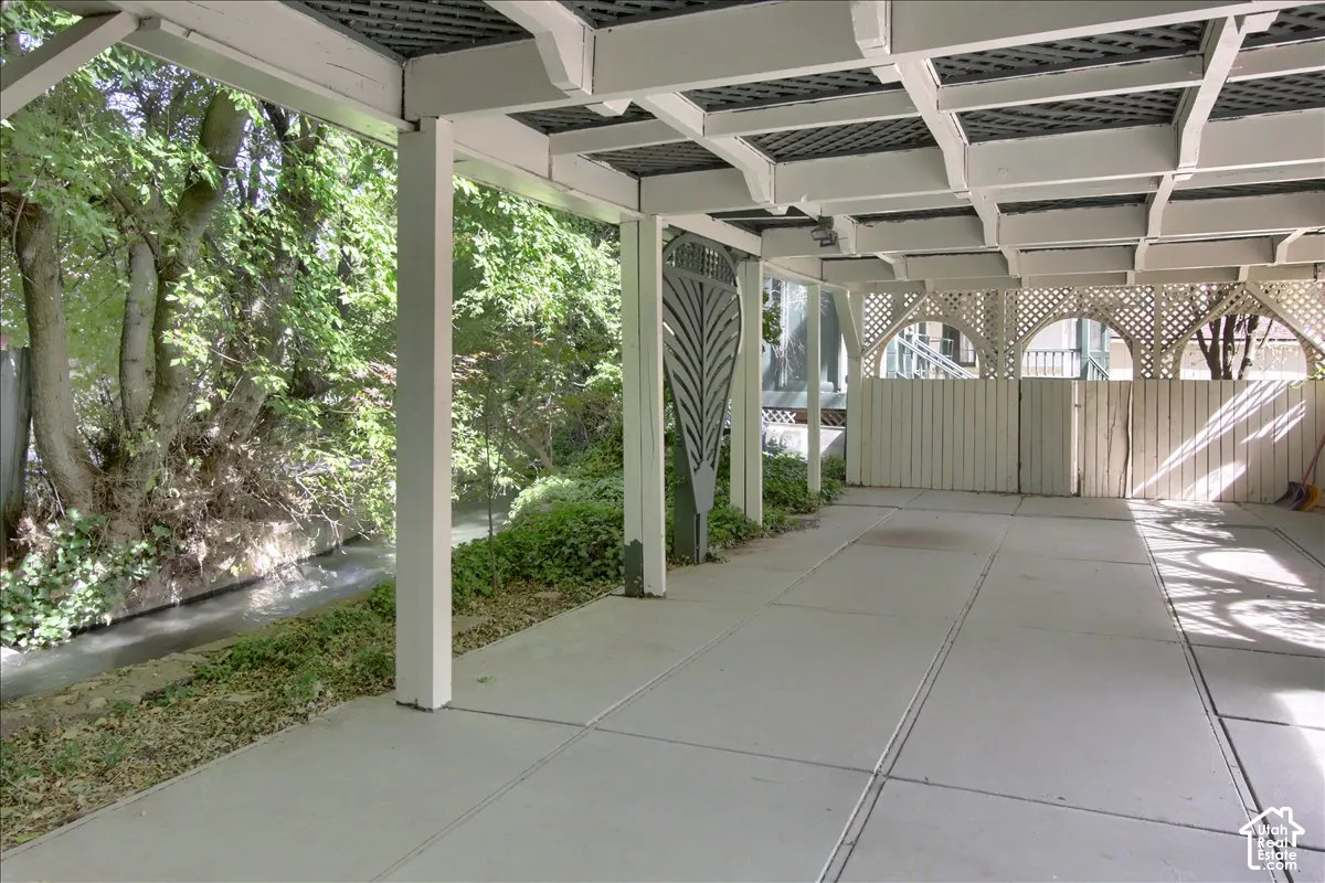 Covered outdoor patio with a concrete surface, featuring a trellis design and wood privacy fencing