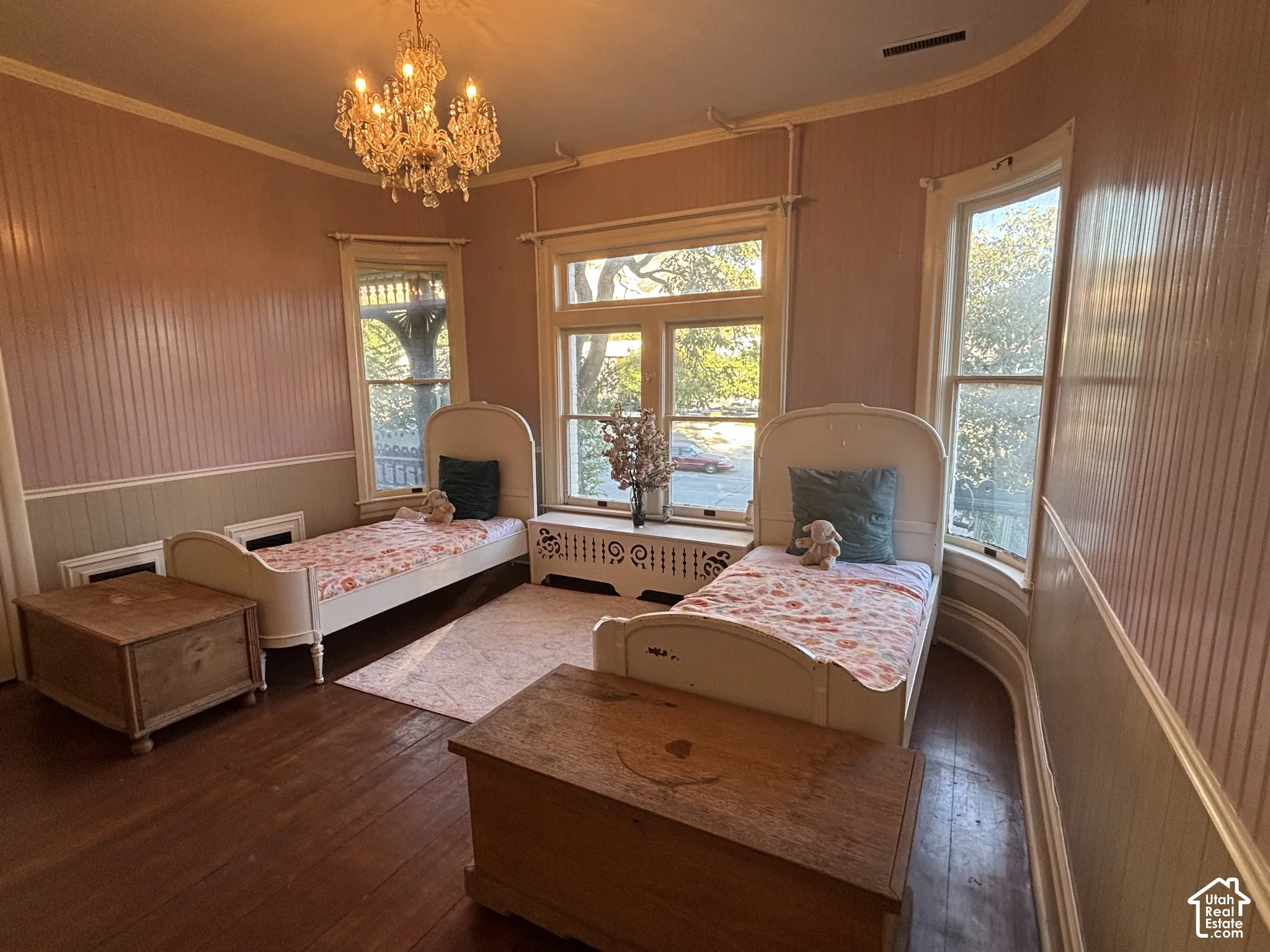 Room featuring beadboard wainscoting, wood-finish flooring, a multi-tiered crystal chandelier, and a curved wall with large windows