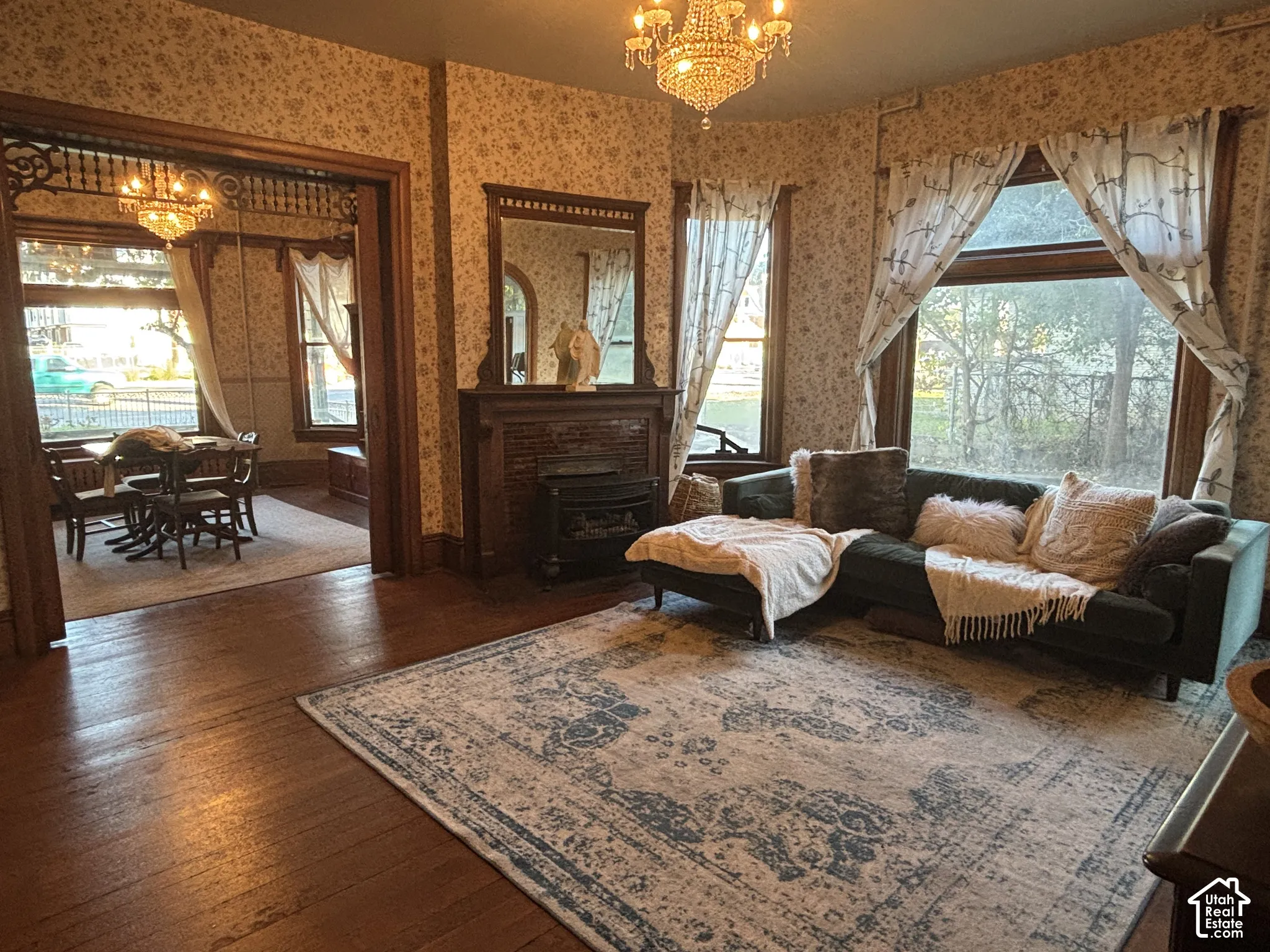 Hardwood flooring, ornate wood-framed fireplace with built-in mirror, crystal-style chandelier, and intricate wooden archway detail
