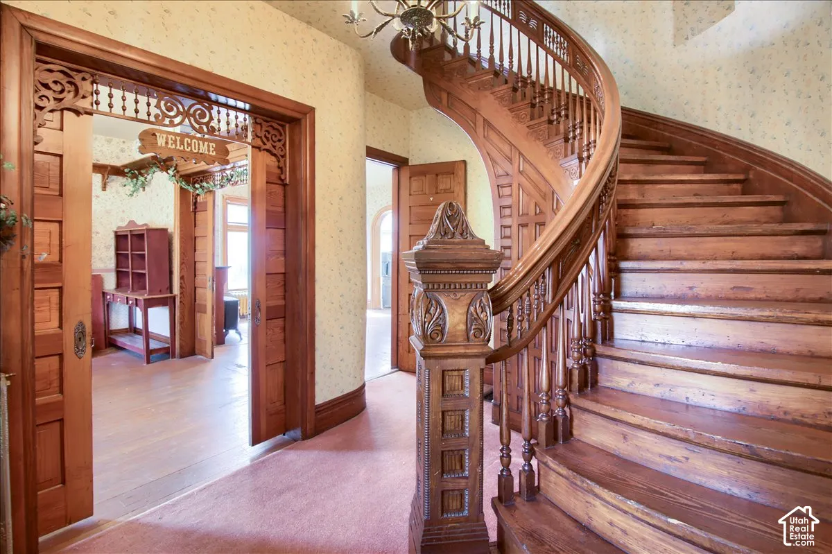 Grand curved staircase with a carved newel post and balusters, featuring a wood-panel accent wall