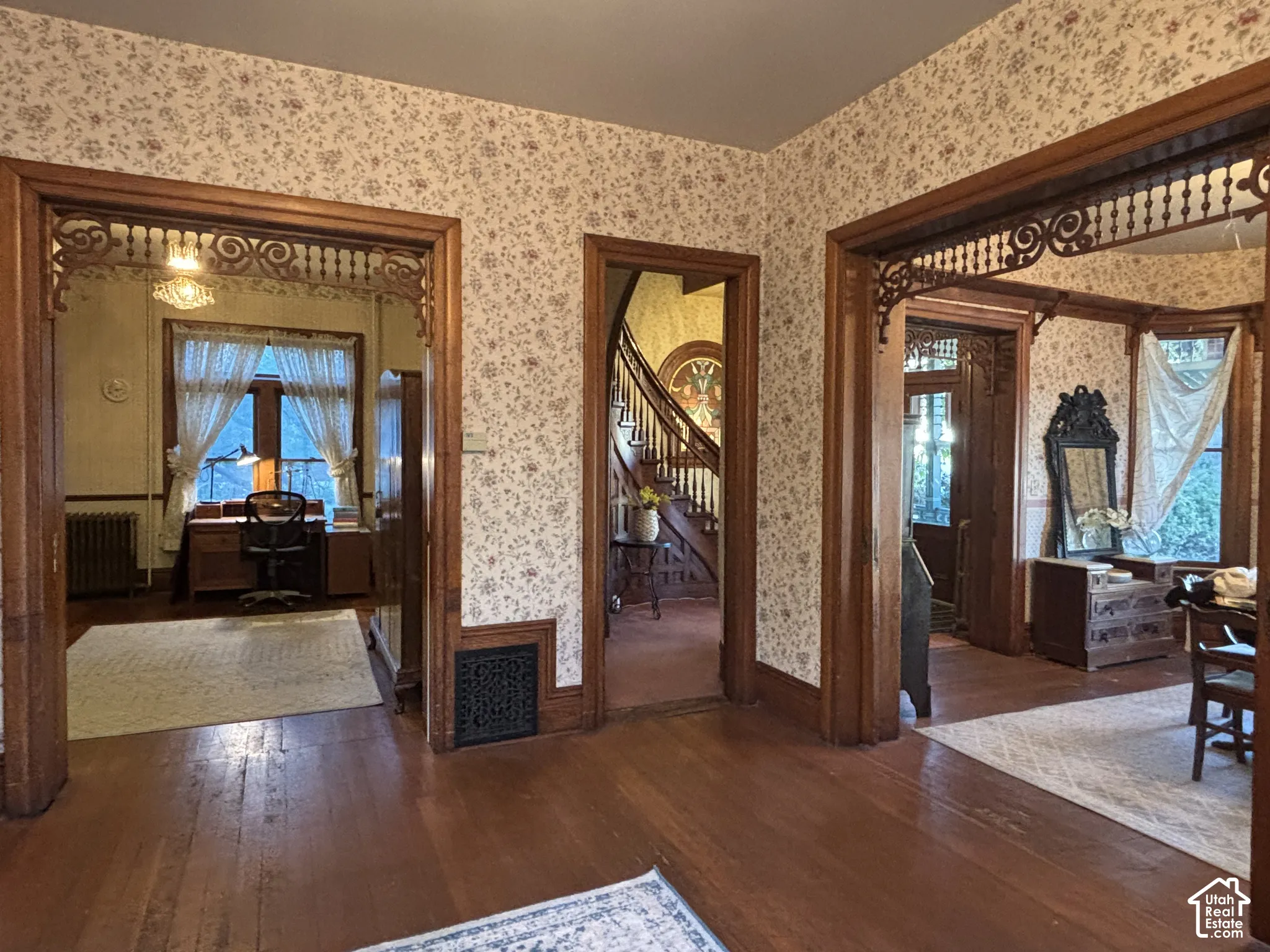 Interior featuring natural wood-finish flooring, ornate woodwork door casings with decorative fretwork, and a staircase with detailed banister detailing