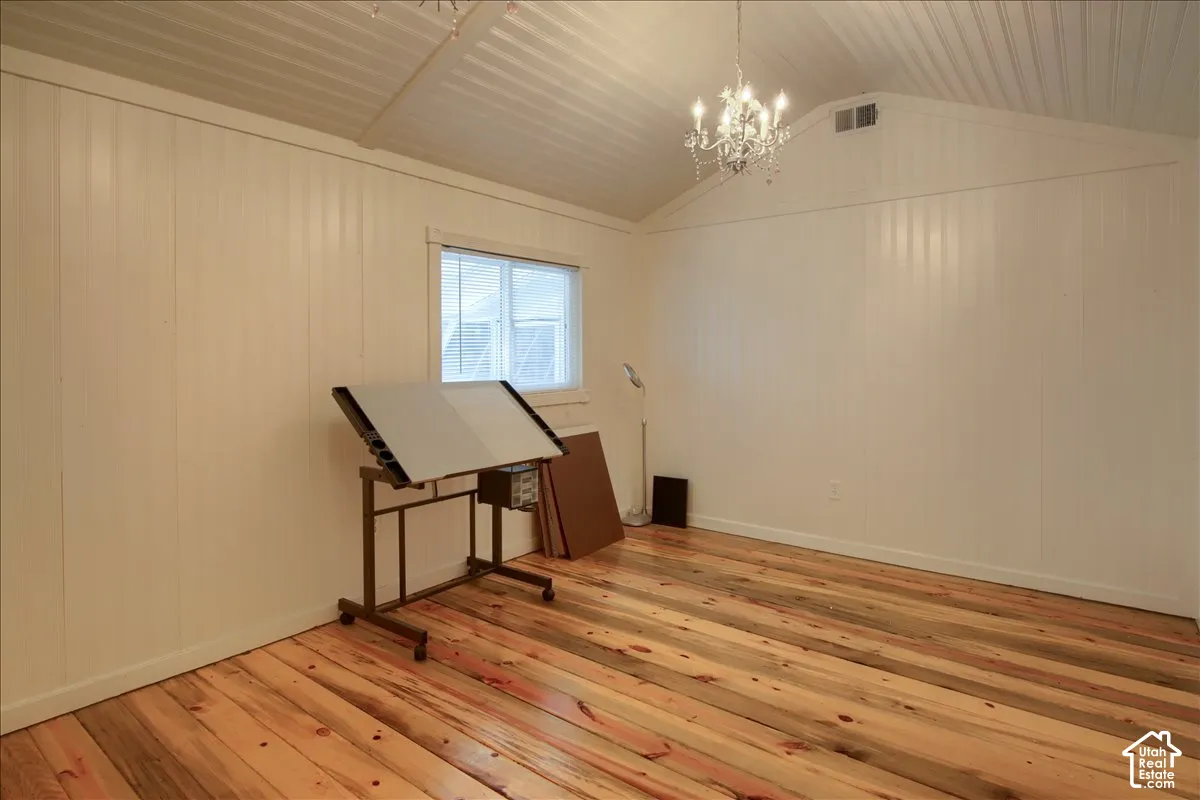 Casita vaulted ceiling with a chandelier, wood-finish flooring, white paneling, and a window with blinds