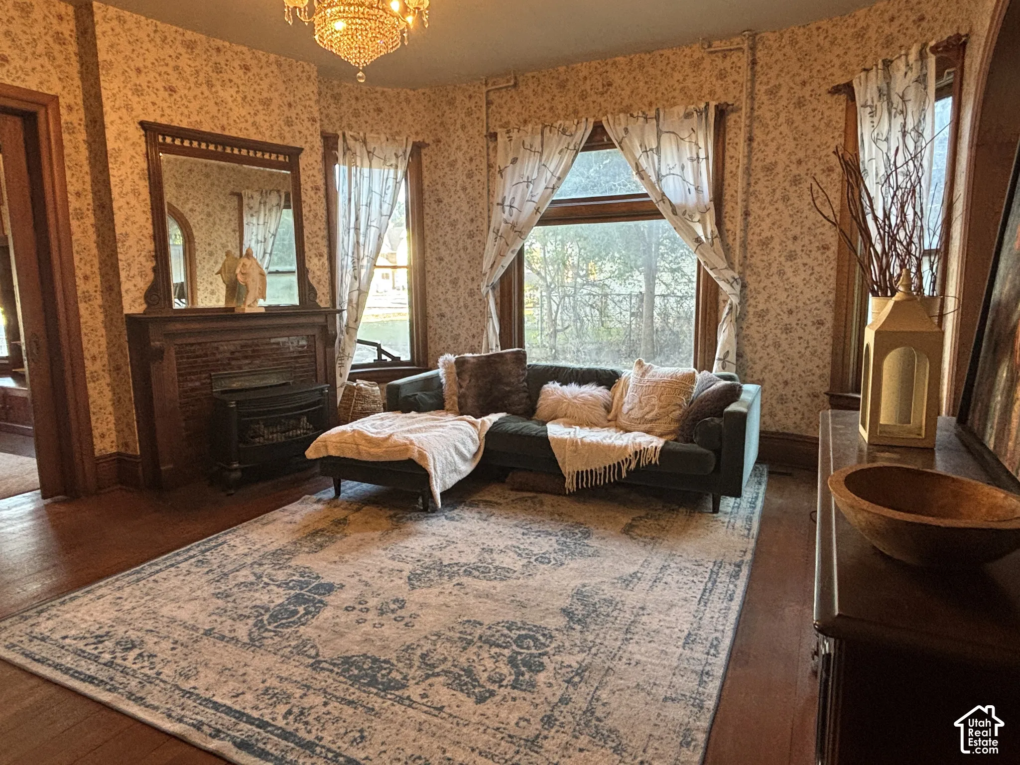 Living area featuring wood-finish flooring, a wood-surround fireplace with an integrated mirror, multi-pane bay windows, and a crystal chandelier