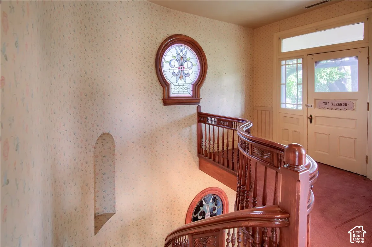 Curved wood staircase with turned balusters, framed by patterned wallpaper