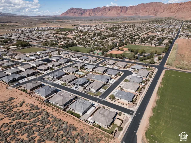 Aerial perspective of a residential neighborhood featuring paved asphalt roadways, concrete driveways, residential structures with shingle roofing, and a backdrop of red rock mountain formations