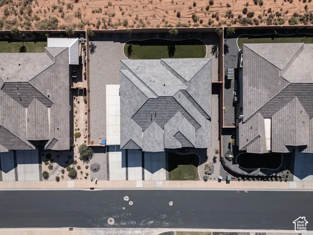 Aerial perspective of a property featuring a tile roof, concrete driveway, front and rear grass lawns, and decorative stone landscaping enclosed by perimeter walls