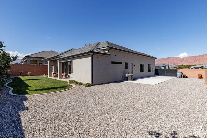 Stucco exterior residence featuring a covered patio, manicured lawn with curved concrete edging, extensive gravel landscaping, and a mountain backdrop