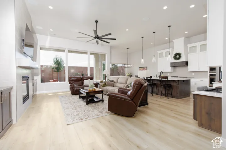 Open-concept living space featuring wood-finish flooring, a linear gas fireplace with a floor-to-ceiling surround, large windows, recessed lighting, and a kitchen island with pendant fixtures