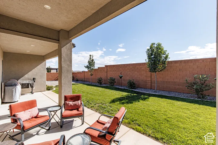 Covered concrete patio featuring recessed lighting, expansive grass lawn, and masonry perimeter wall with integrated landscaping