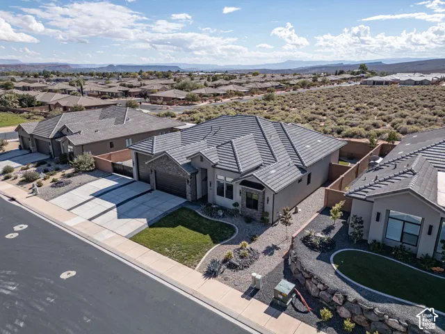 Single-level stucco exterior featuring a tile roof, stone masonry accents, a three-car garage, and landscaped front yard with desert rock elements