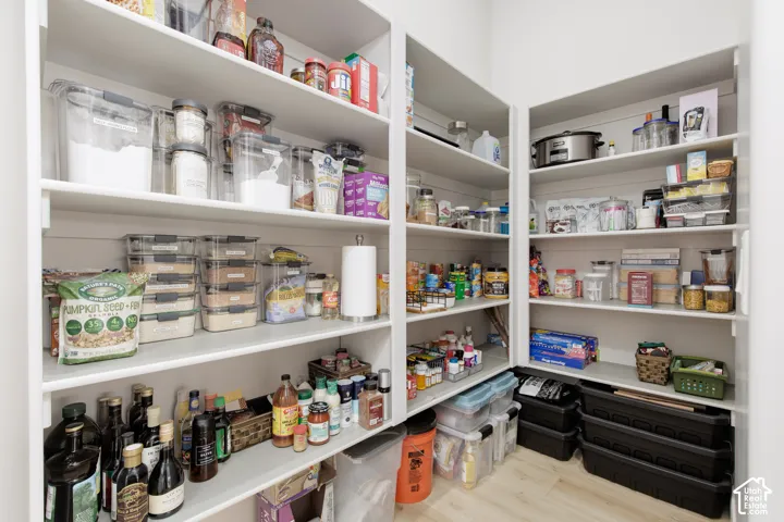 Walk-in pantry featuring white floor-to-ceiling built-in shelving, horizontal shiplap wall detailing, and light wood-finish flooring