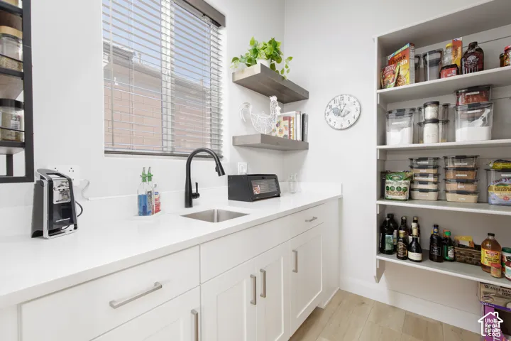 Custom pantry featuring white cabinetry, solid surface countertops, an undermount sink with a matte black faucet, open wood-finish shelving, and wood-finish flooring