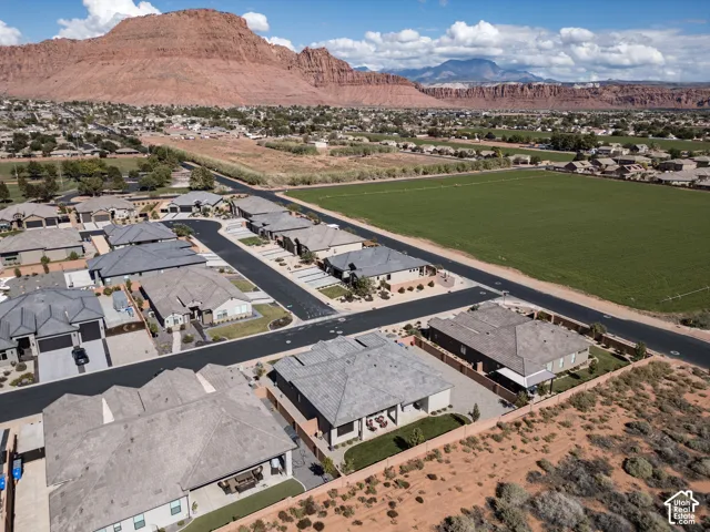 Aerial perspective of a residential neighborhood featuring prominent red rock mountain scenery, paved streets, and expansive open green space