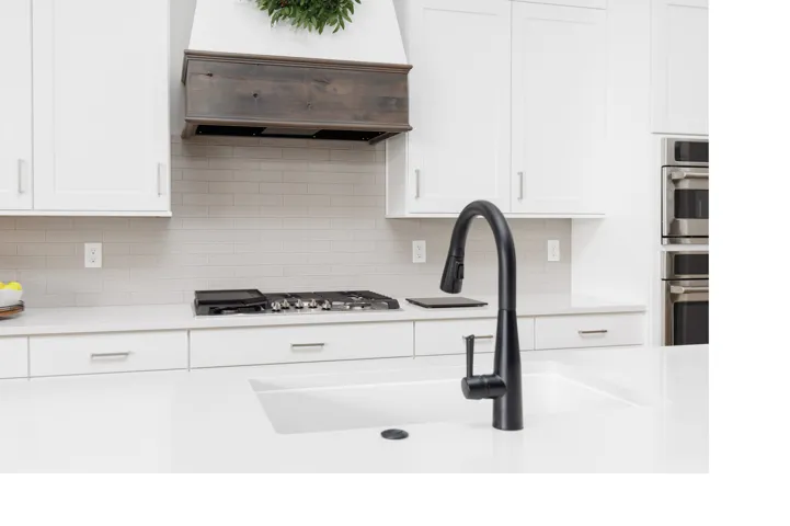 Kitchen featuring white cabinetry, a wood-finish range hood, light-toned tile backsplash, quartz countertops, and a matte black gooseneck faucet