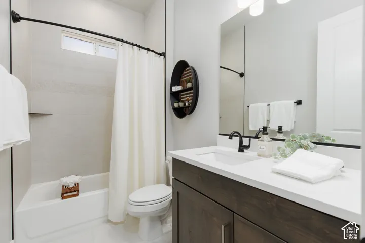 Bathroom featuring a vanity with wood-finish cabinetry, a white countertop, matte black fixtures, and a shower-tub combination with light-toned wall tile