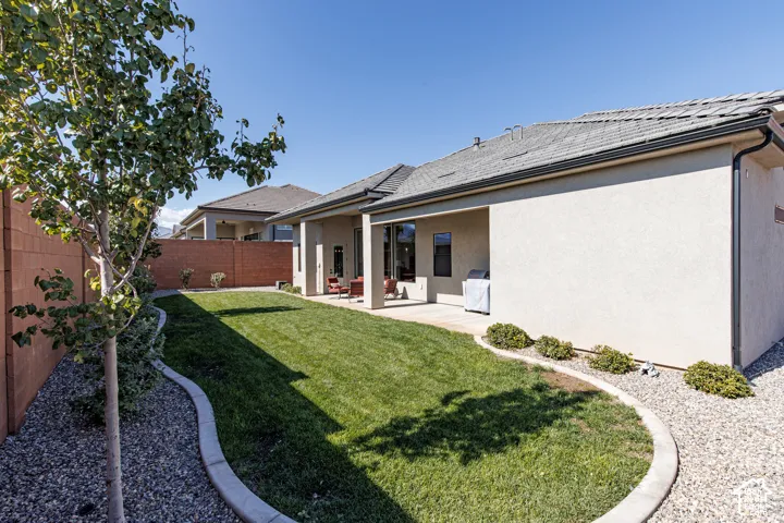 Stucco exterior featuring a covered concrete patio, enclosed backyard with a manicured lawn, curved concrete curbing, and a perimeter masonry wall