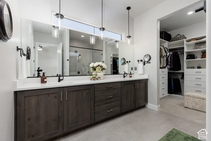 Dual-sink vanity featuring dark wood-finish cabinetry, quartz countertops, pendant lighting, and a large-format mirror with integrated transom window