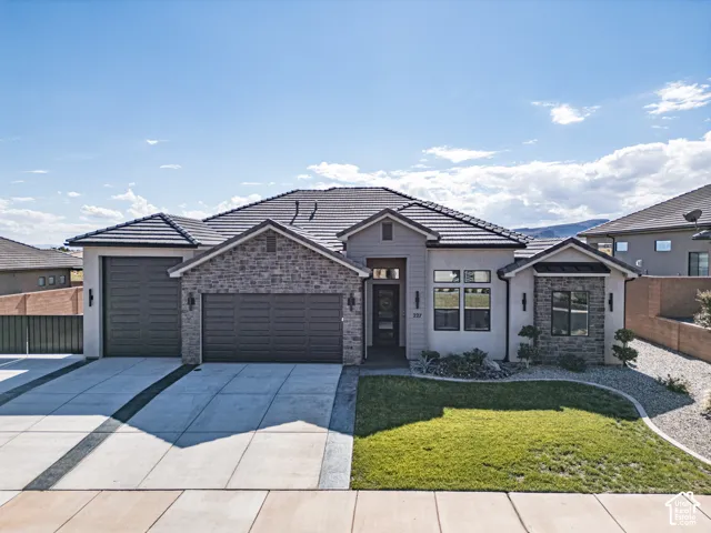 Single-story residence featuring a stone and stucco facade, concrete tile roof, multi-car garage, and manicured front lawn with xeriscape landscaping