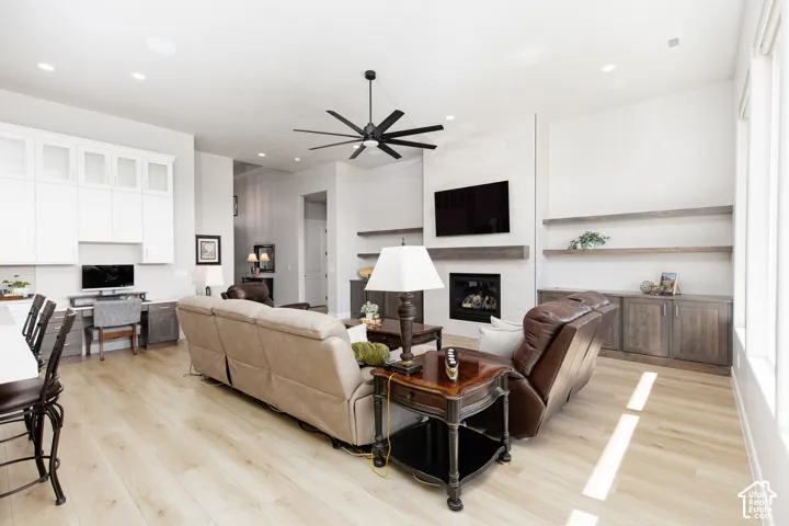 Living area featuring wood-finish flooring, a fireplace with a horizontal stone surround, built-in cabinetry with integrated workspace, recessed lighting, and a multi-blade ceiling fan