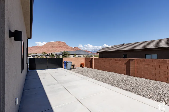 Exterior side yard featuring a concrete patio, stone ground cover, a masonry perimeter wall, and a black metal gate, complemented by mountain scenery