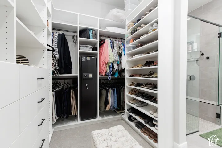 Walk-in closet featuring floor-to-ceiling white built-in shelving, custom drawer units with matte black hardware, integrated hanging rods, and an enclosed glass shower stall with tiled surround