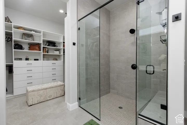 Walk-in shower featuring large-format tile surround, glass enclosure, built-in bench, and matte black fixtures, complemented by custom built-in white cabinetry