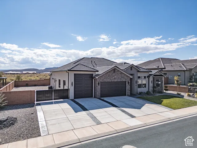 Single-story exterior featuring a stucco finish, stone veneer accents, multi-car garage, concrete driveway, and side-yard gated access