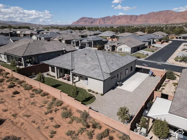 Stucco exterior with a multi-hip tile roof, enclosed backyard, concrete patio, gravel side yard, and mountain backdrop