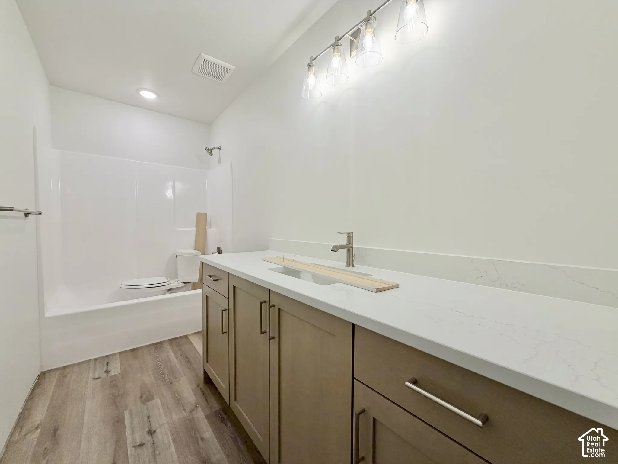 Bathroom featuring an extended vanity with stone-style countertop and undermount sink, shaker-style cabinetry, four-light vanity fixture, and wood-finish flooring