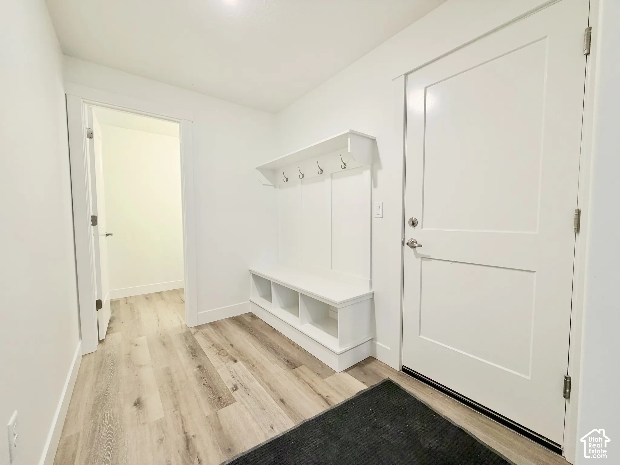 Entryway featuring wood-finish flooring, a white paneled door, and built-in white cabinetry with integrated wall hooks and lower storage cubbies