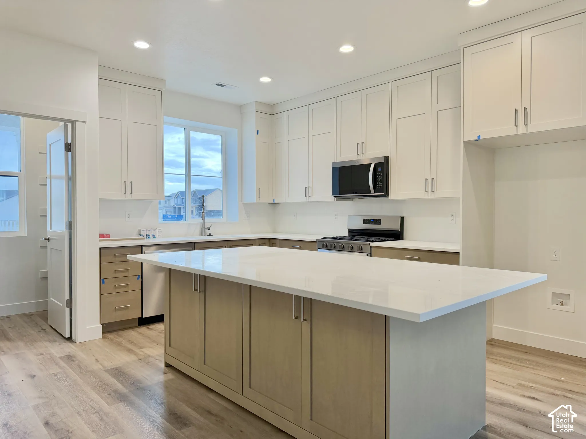 Kitchen featuring two-tone shaker-style cabinetry, quartz countertops, a central island, recessed lighting, and wood-finish flooring