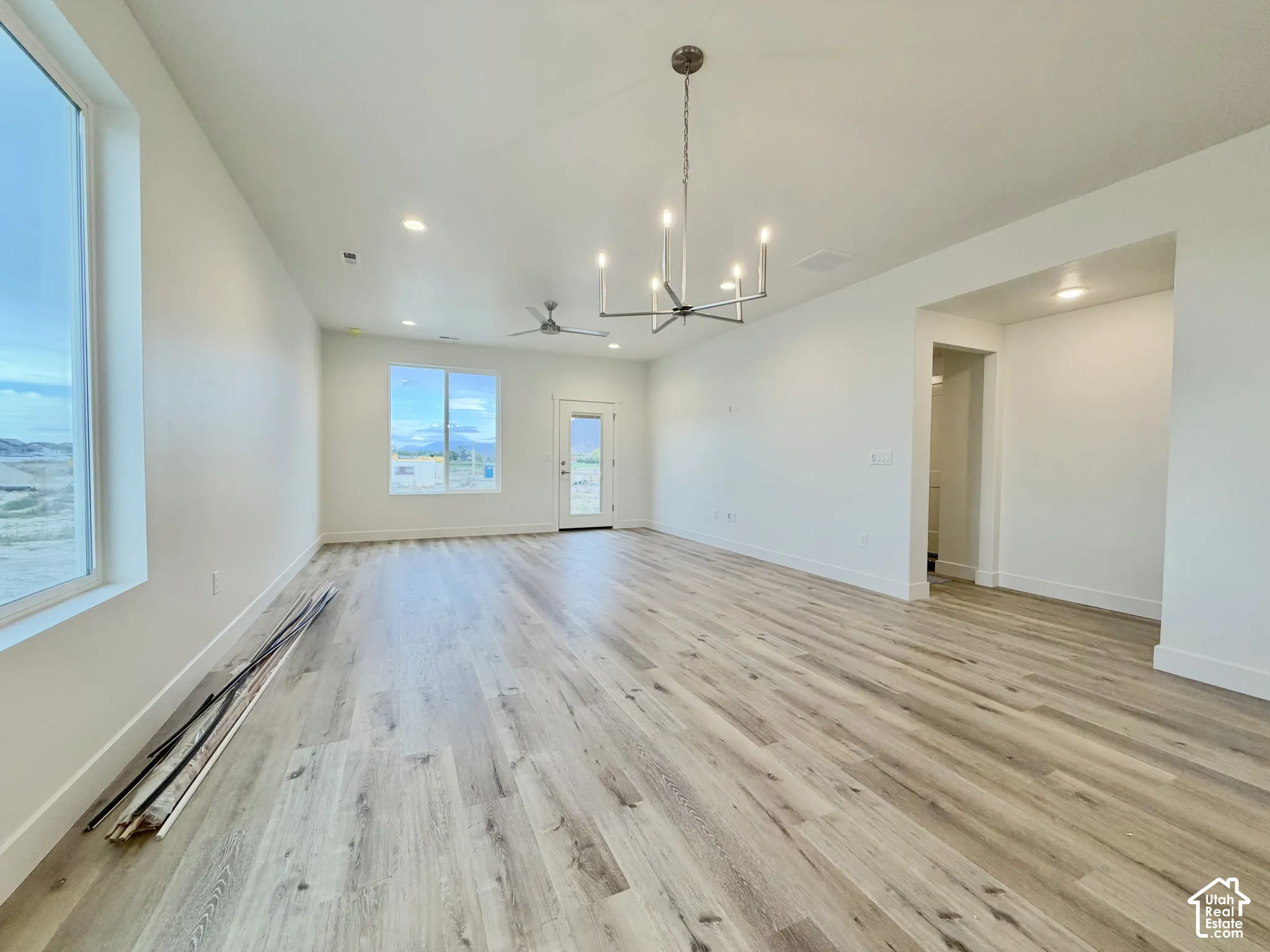 Open-concept interior featuring wood-finish flooring, a modern multi-arm chandelier, recessed lighting, and large windows